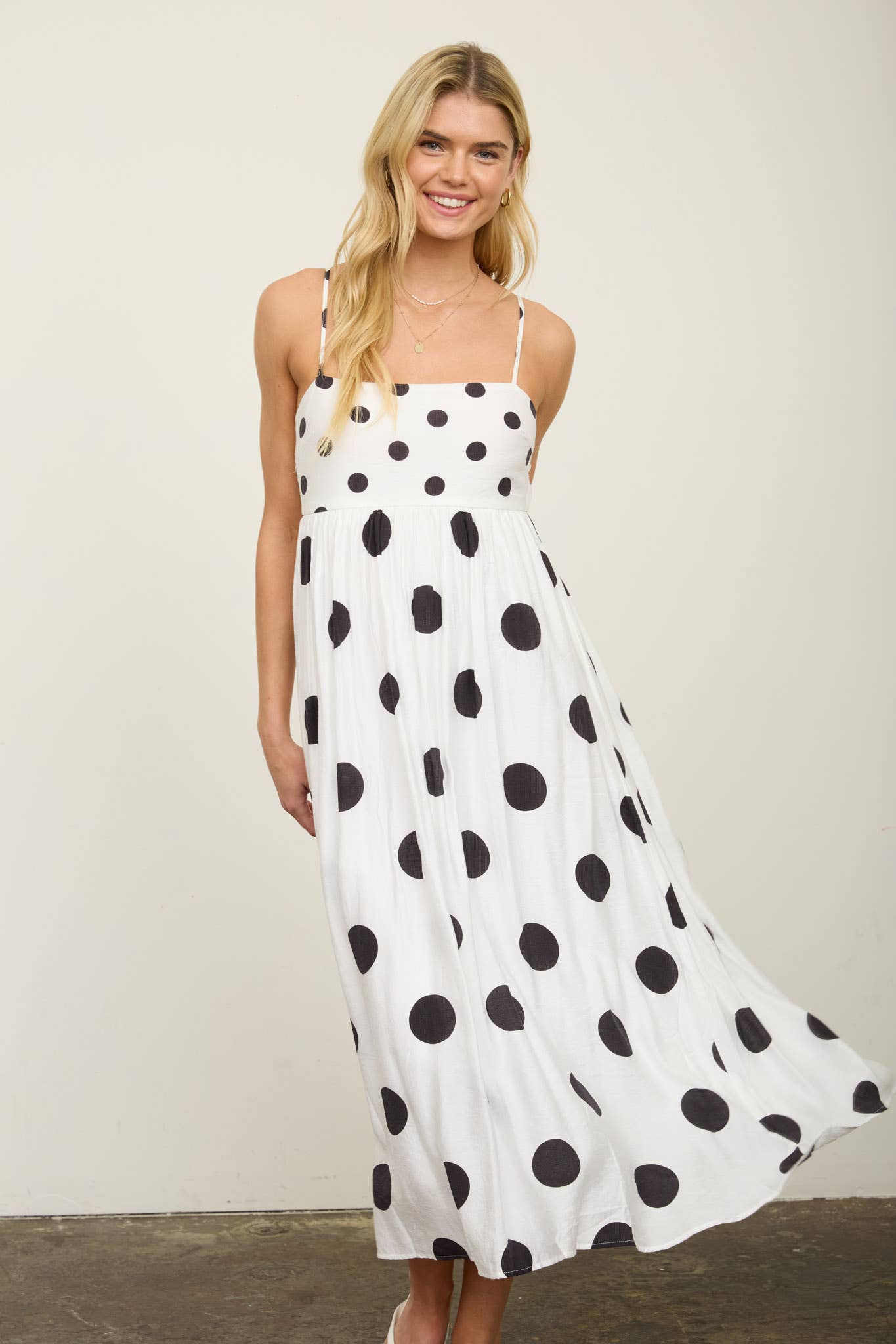 Woman wearing a white dress with black polka dots against a plain background