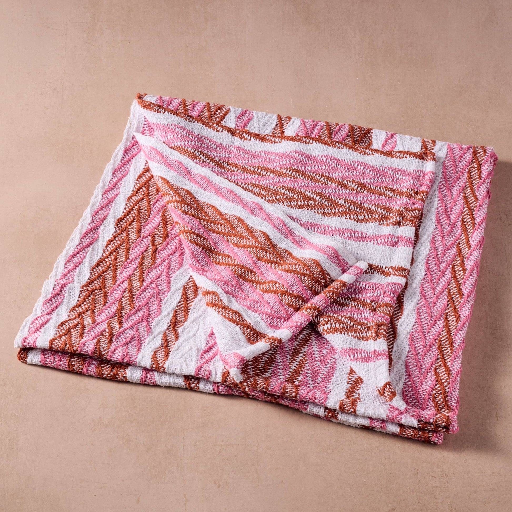 Folded pink and brown patterned towel on a beige background