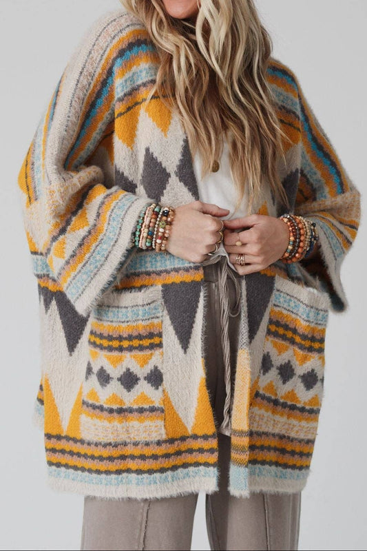 Woman wearing a patterned poncho and knit hat on a plain background