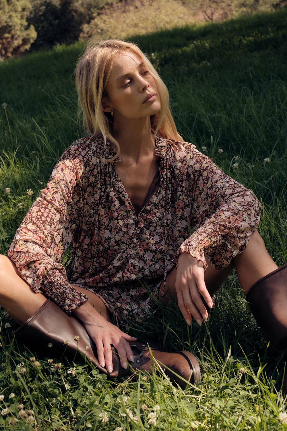 Woman sitting on grass wearing a floral blouse