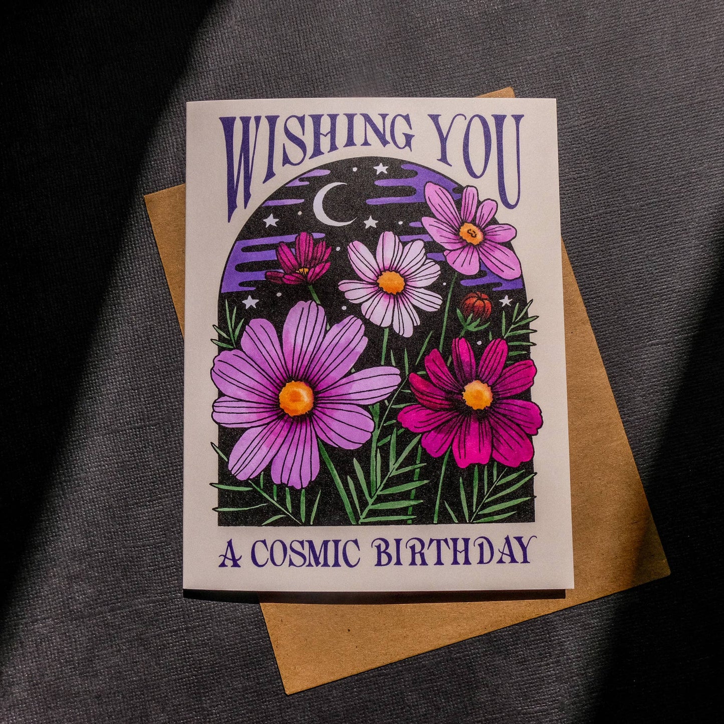 Greeting card with purple and pink flowers and 'Wishing you a cosmic birthday' text on a dark background.