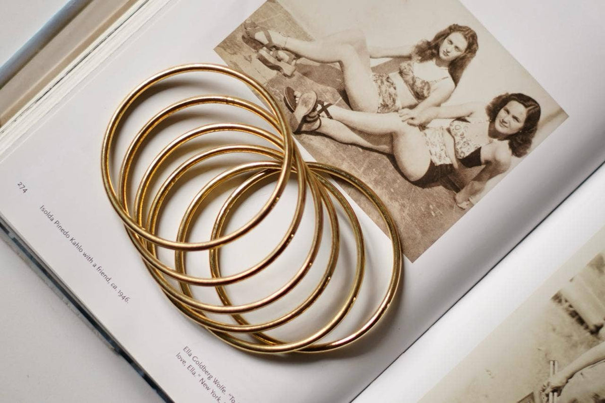 Five interlocked gold bangles stacked on an open book with vintage photographs.