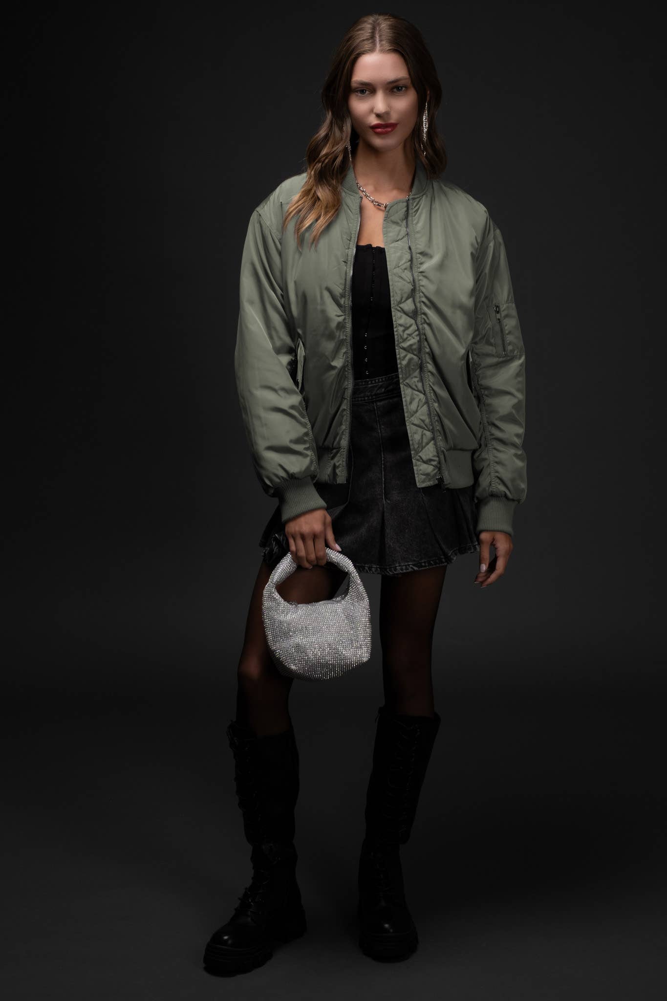 Woman wearing a green jacket and black outfit holding a white fur bag against a dark background