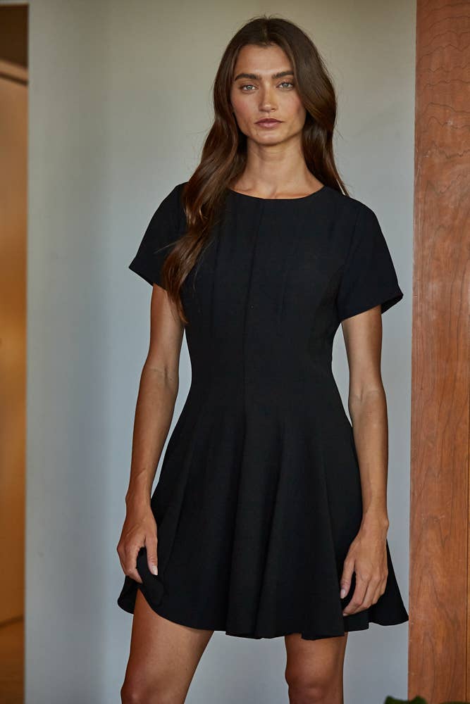 Woman wearing a black dress standing against a neutral background