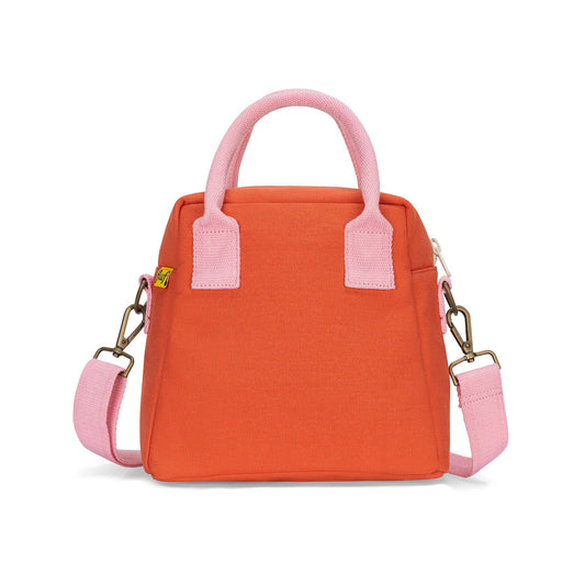 An orange canvas handbag with light pink handles, trim, and a matching shoulder strap, shown against a plain white background.