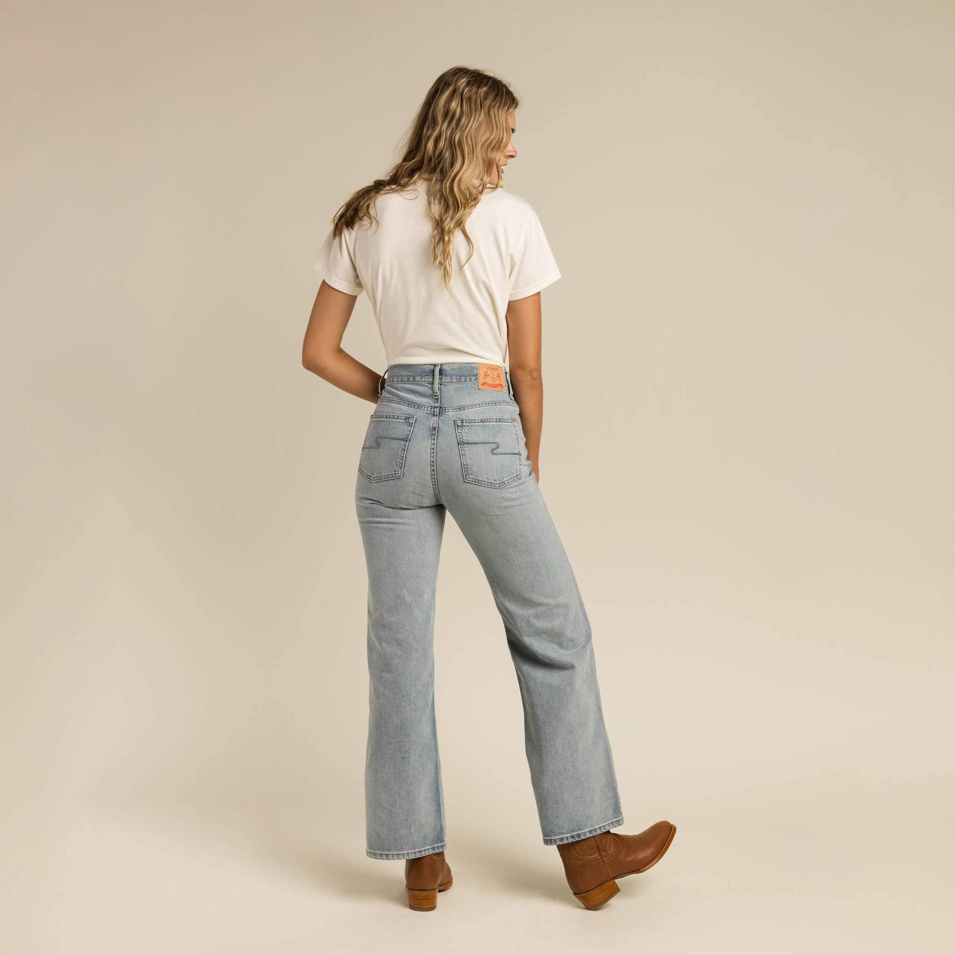 Woman wearing light blue jeans and a white t-shirt on a beige background