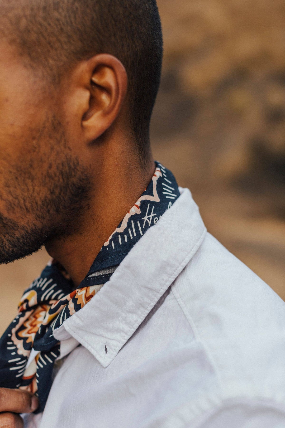 Man wearing a patterned scarf and light-colored shirt with a blurred natural background