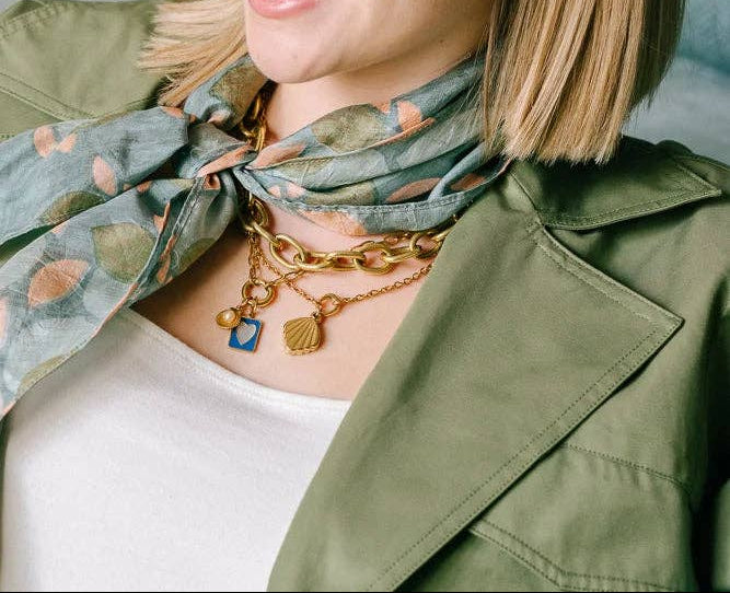 Woman wearing a green jacket with a floral scarf and gold jewelry, smiling.