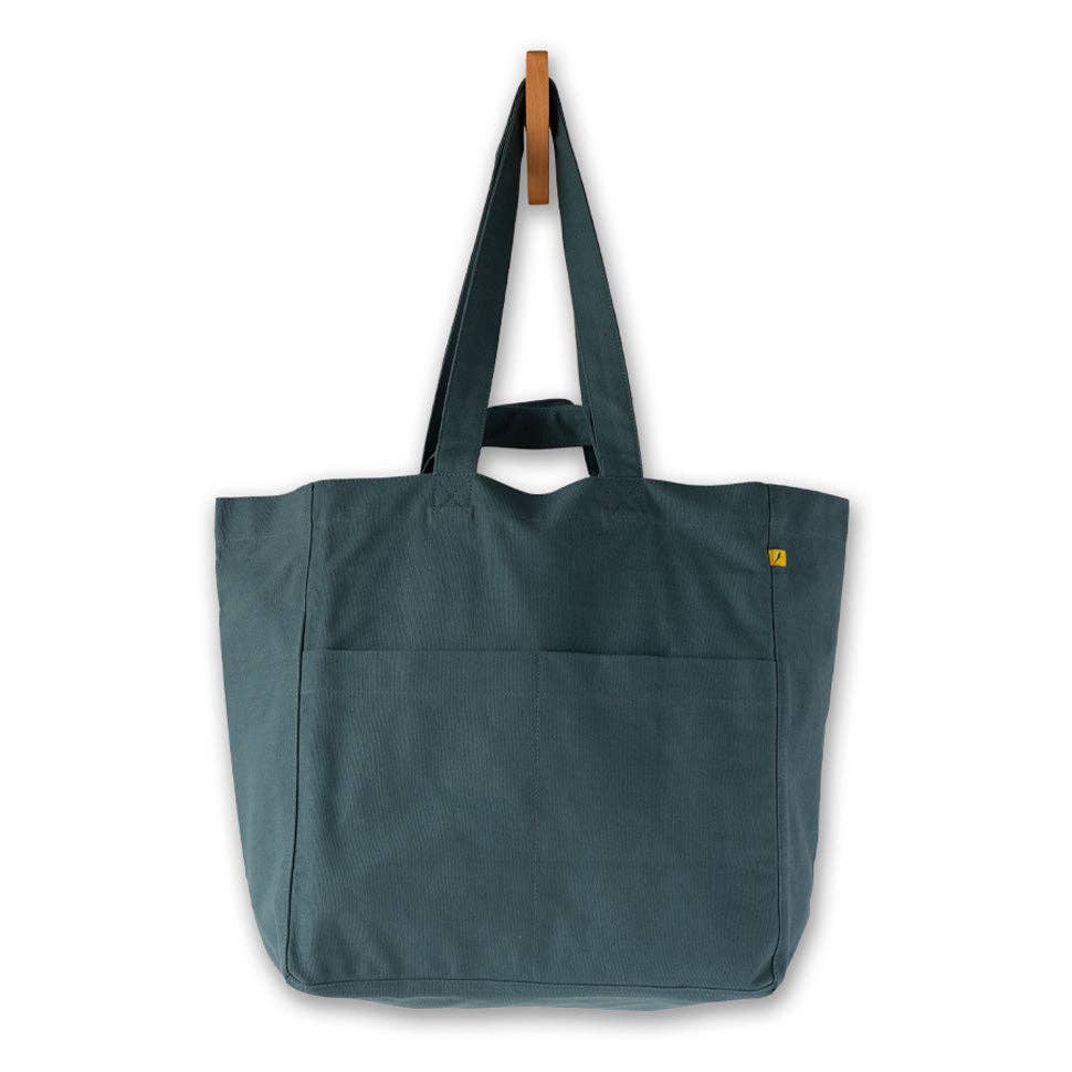 A dark teal canvas tote bag with dual shoulder straps, hanging from a wooden peg on a white background.