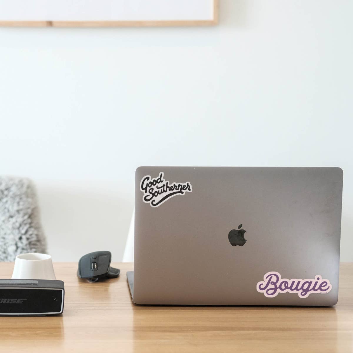 Laptop with stickers on a desk with a Bose device and a white wall in the background