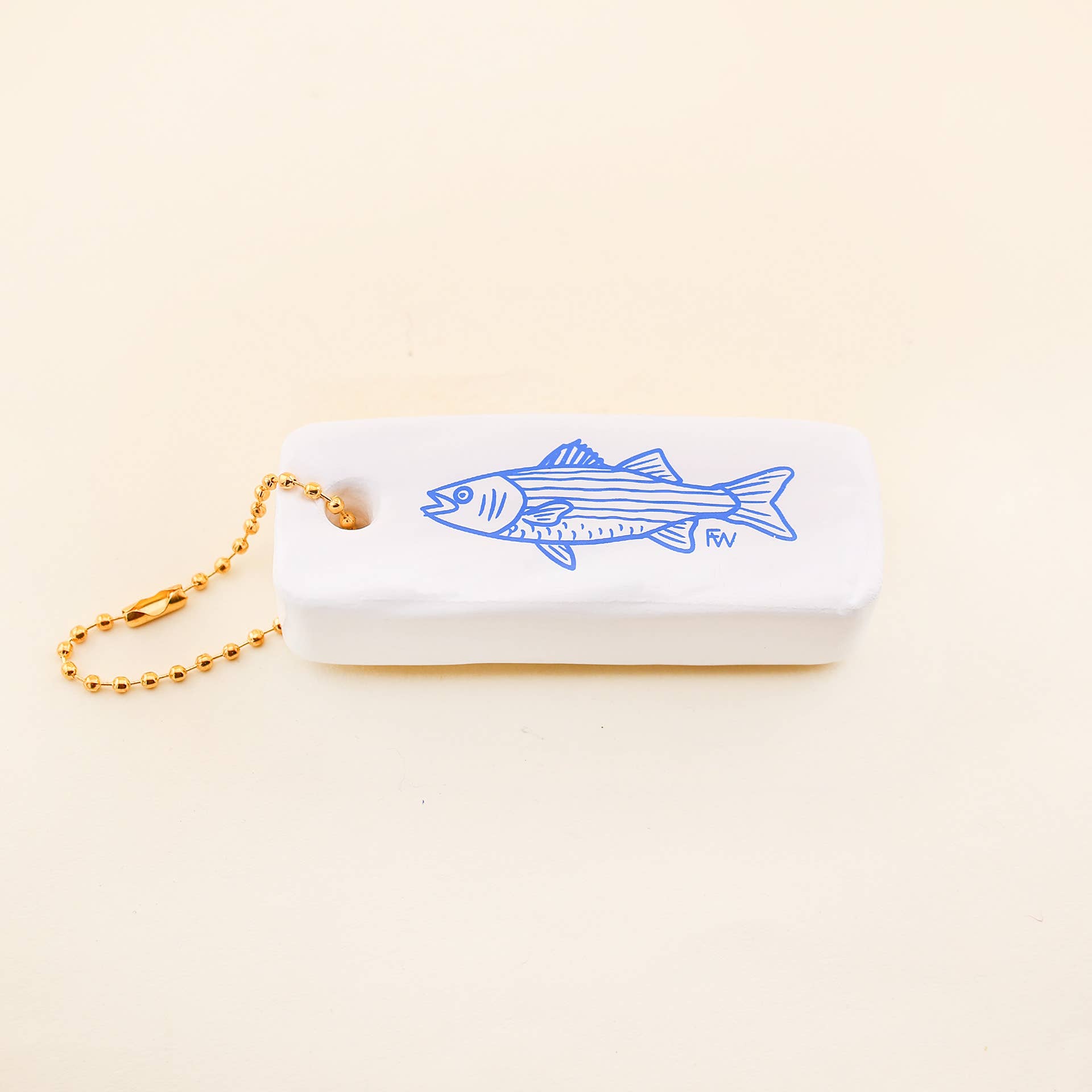 White object with blue fish design and gold chain on beige background