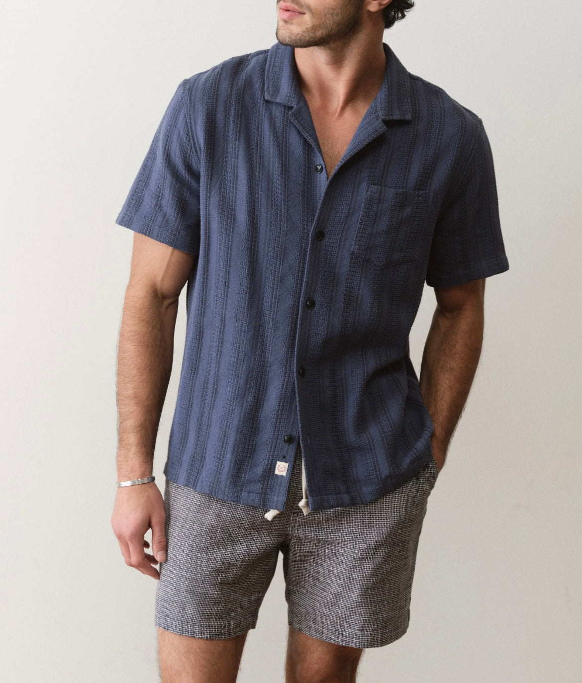 Man wearing a blue striped shirt and gray shorts against a plain background