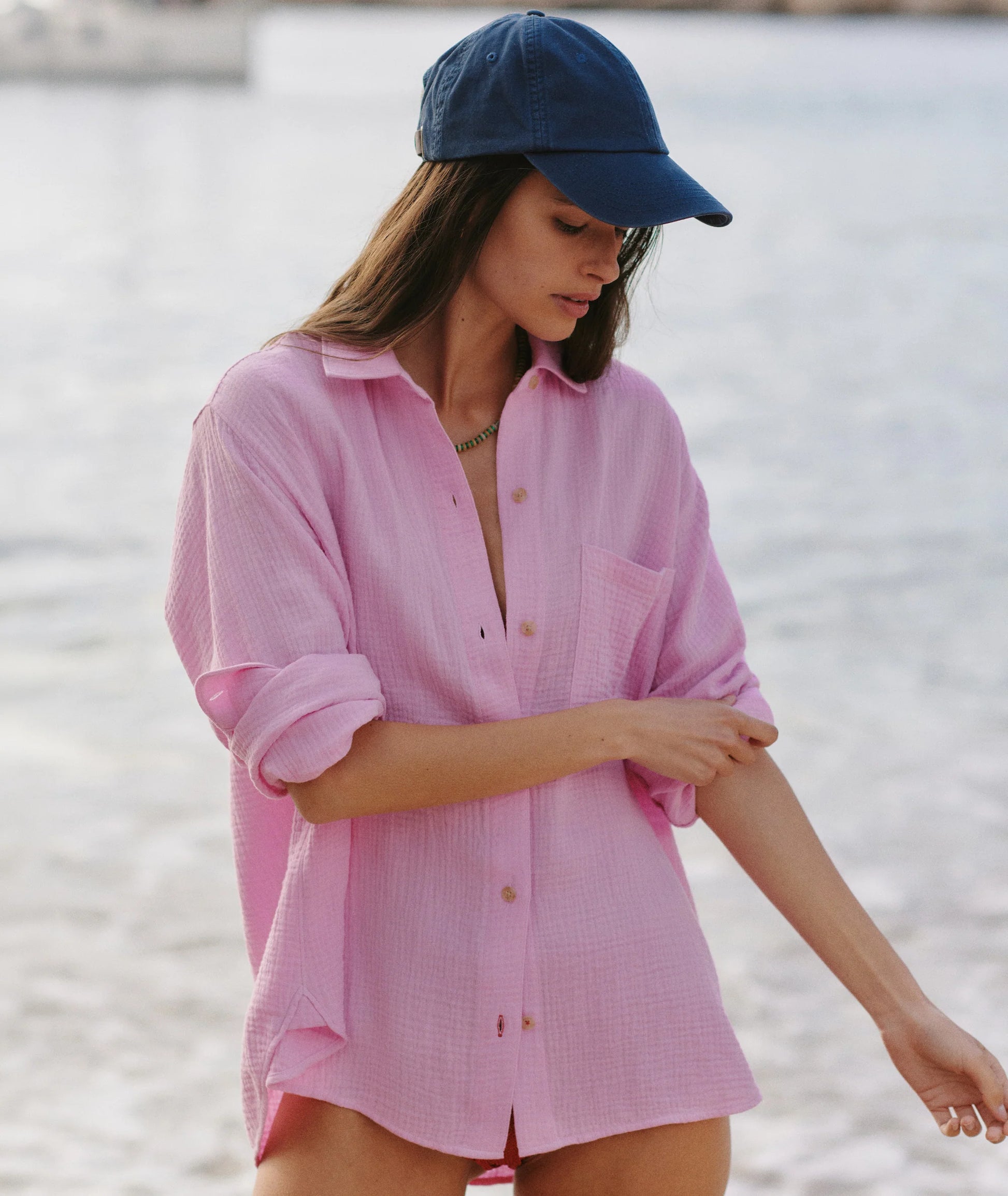 Woman wearing a pink shirt and blue cap by a body of water