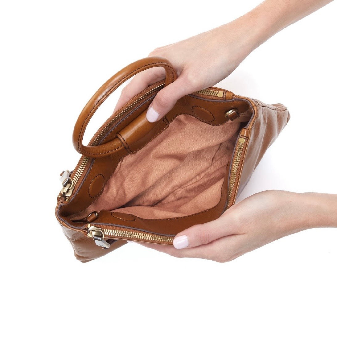 A tan leather handbag with a matching top handle, shown open with a person's hands holding it against a plain white background.