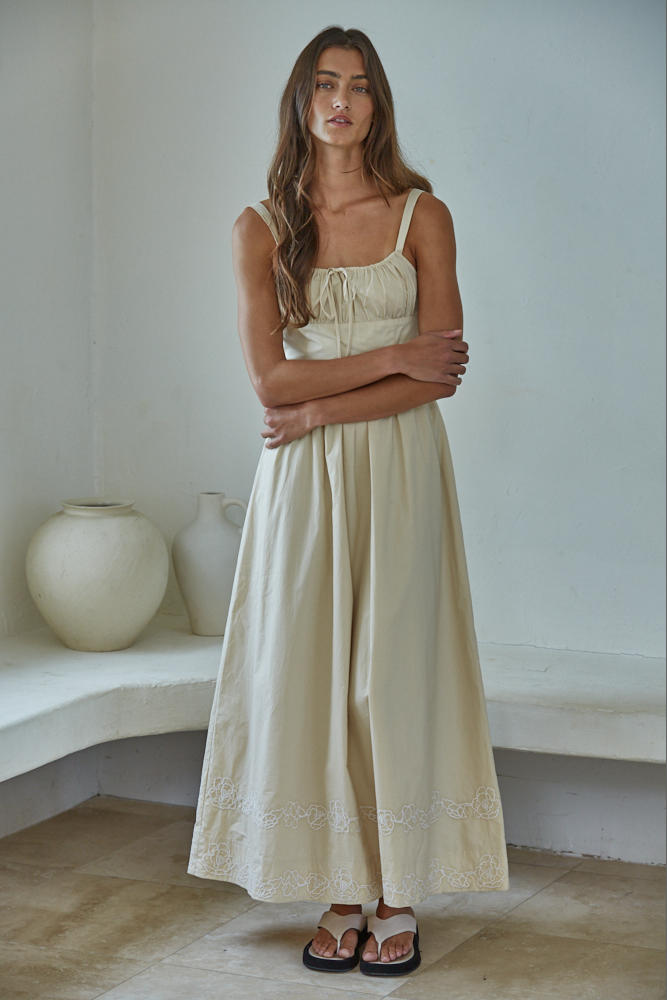 Woman wearing a beige dress standing in a minimalistic room with white walls and a wooden floor.