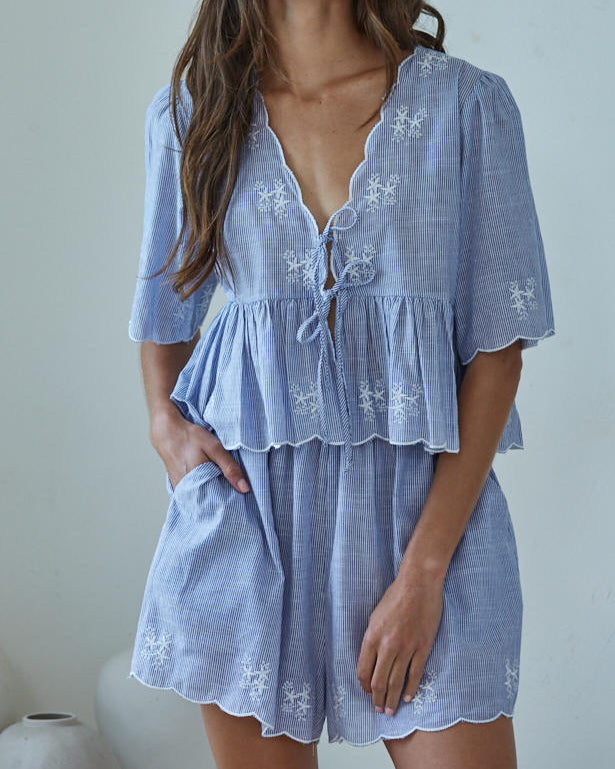 Woman wearing a light blue embroidered dress against a plain background