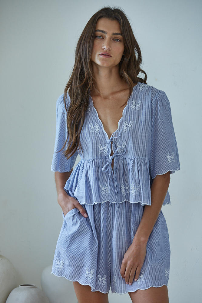 Woman wearing a light blue embroidered dress against a plain background