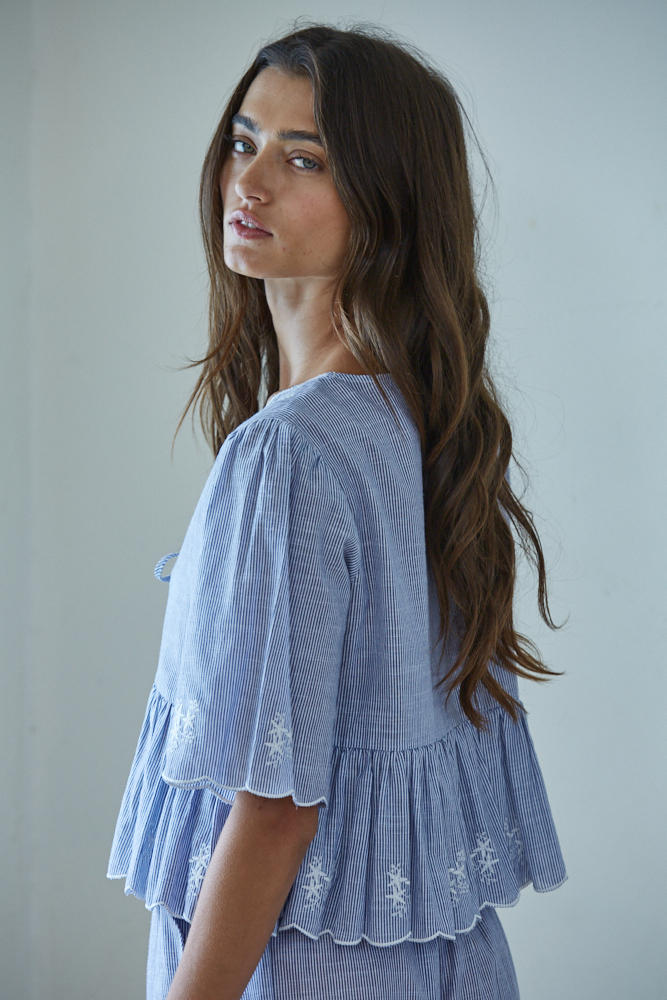 Woman wearing a blue embroidered top against a plain background