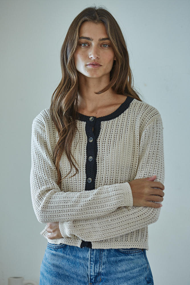 Woman wearing a beige knitted cardigan with a navy collar against a plain background