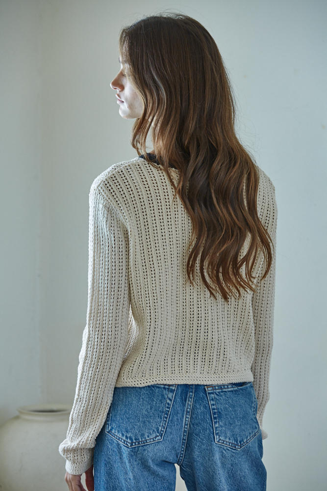 Woman wearing a beige knitted sweater and blue jeans against a plain background