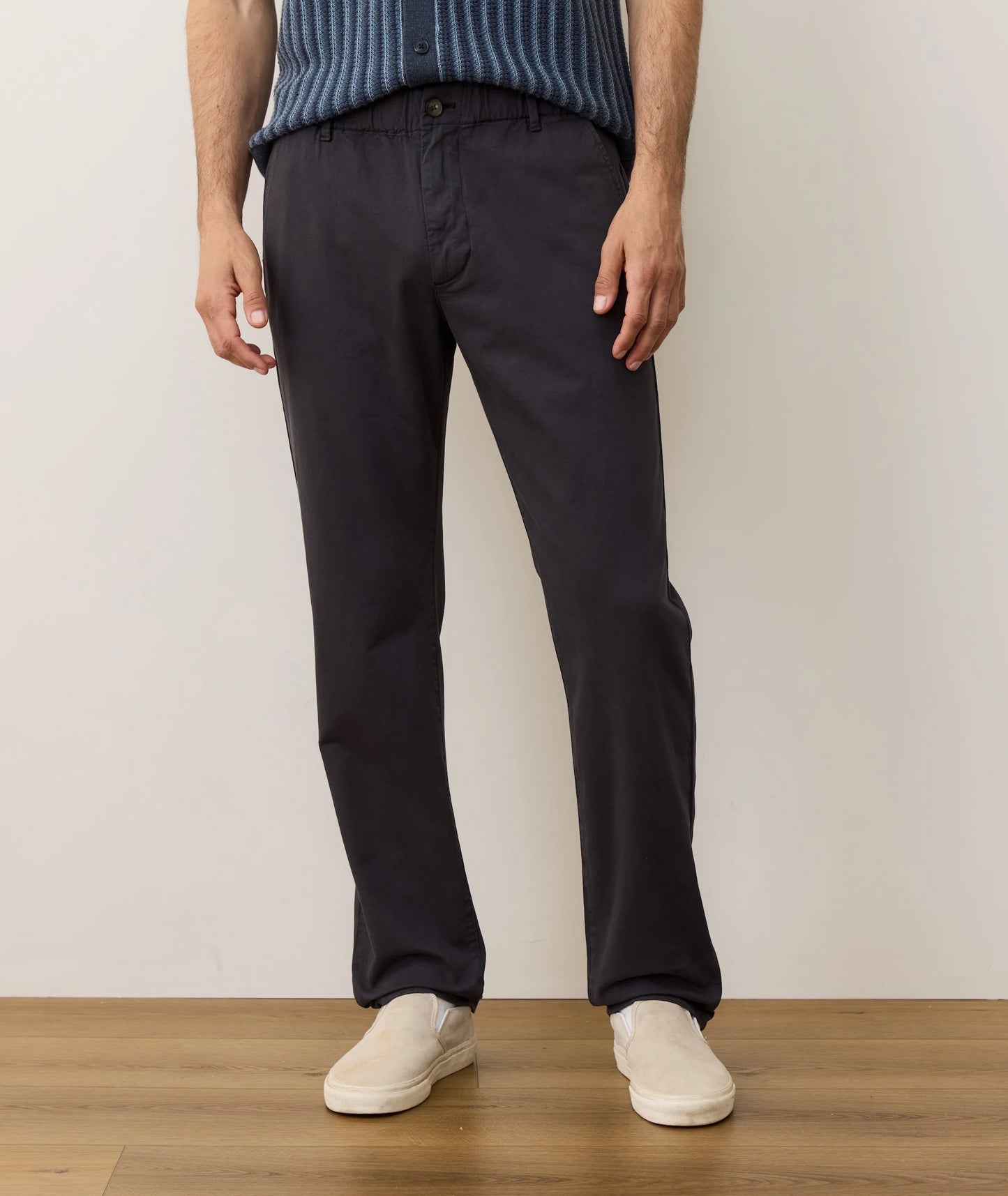 Person wearing black pants and a blue sweater standing against a plain background