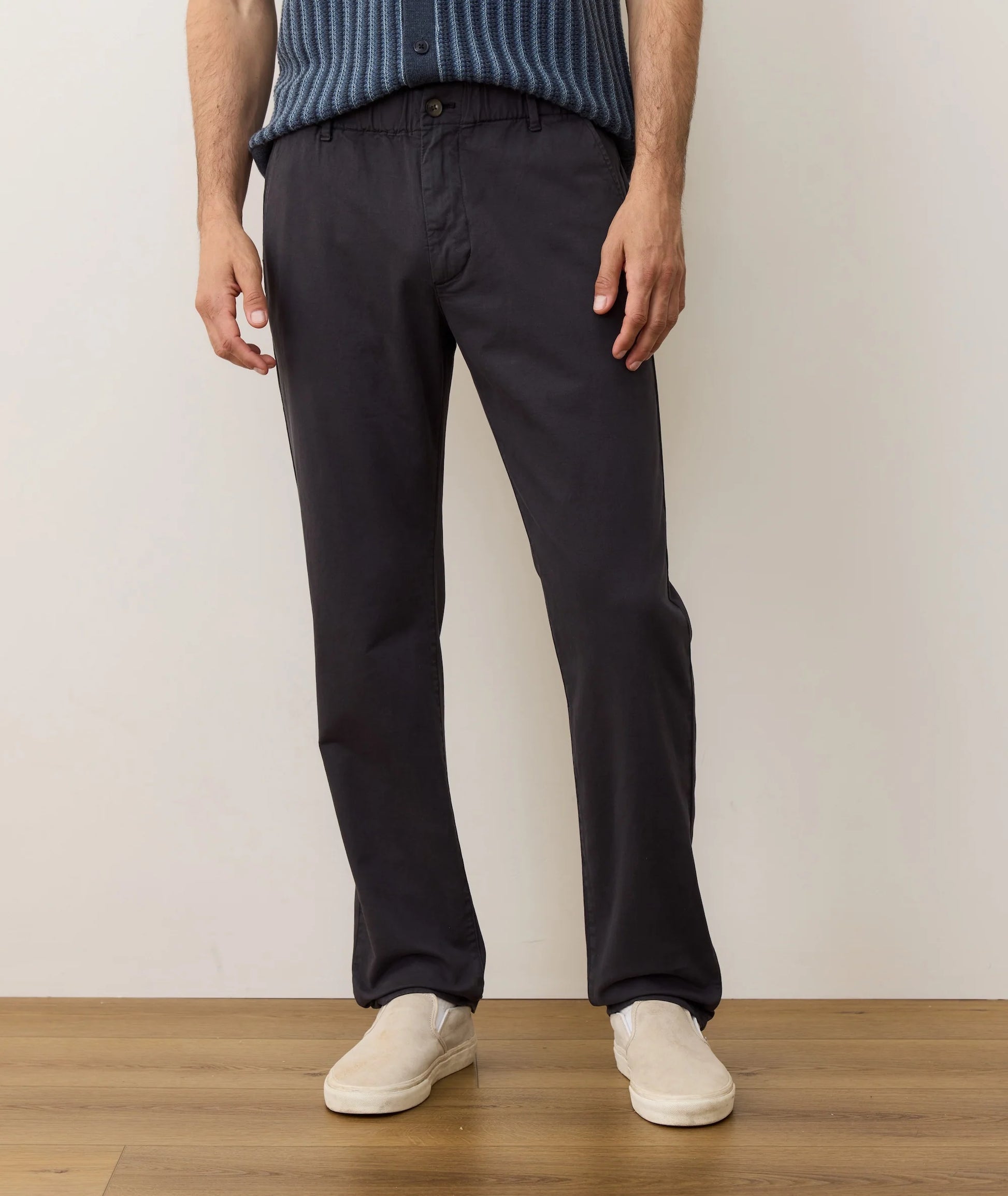 Person wearing black pants and a blue sweater standing against a plain background