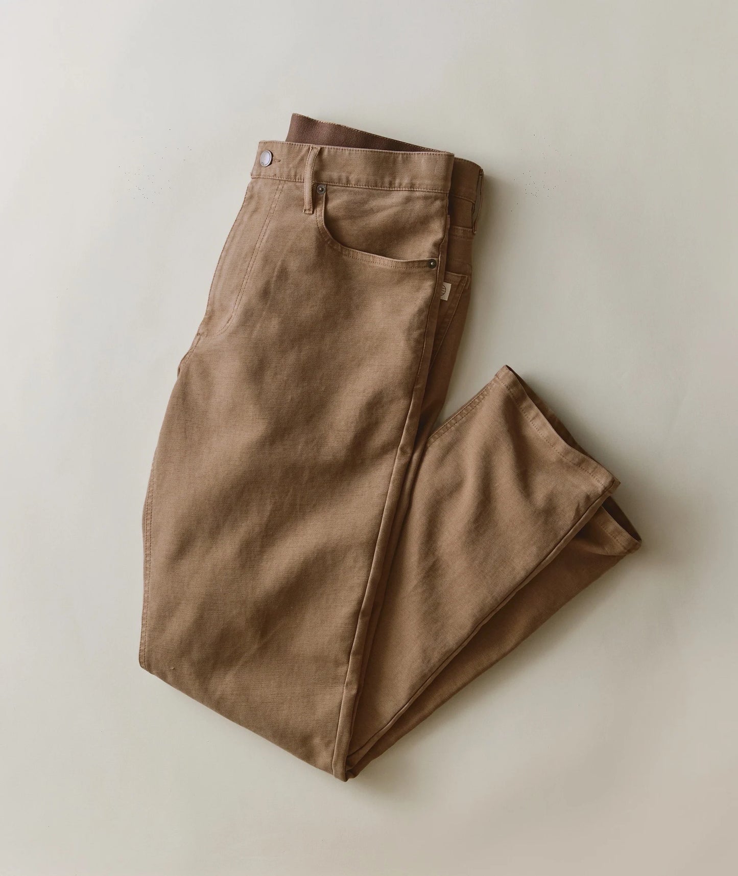 A pair of folded brown trousers laid flat on a light beige background.