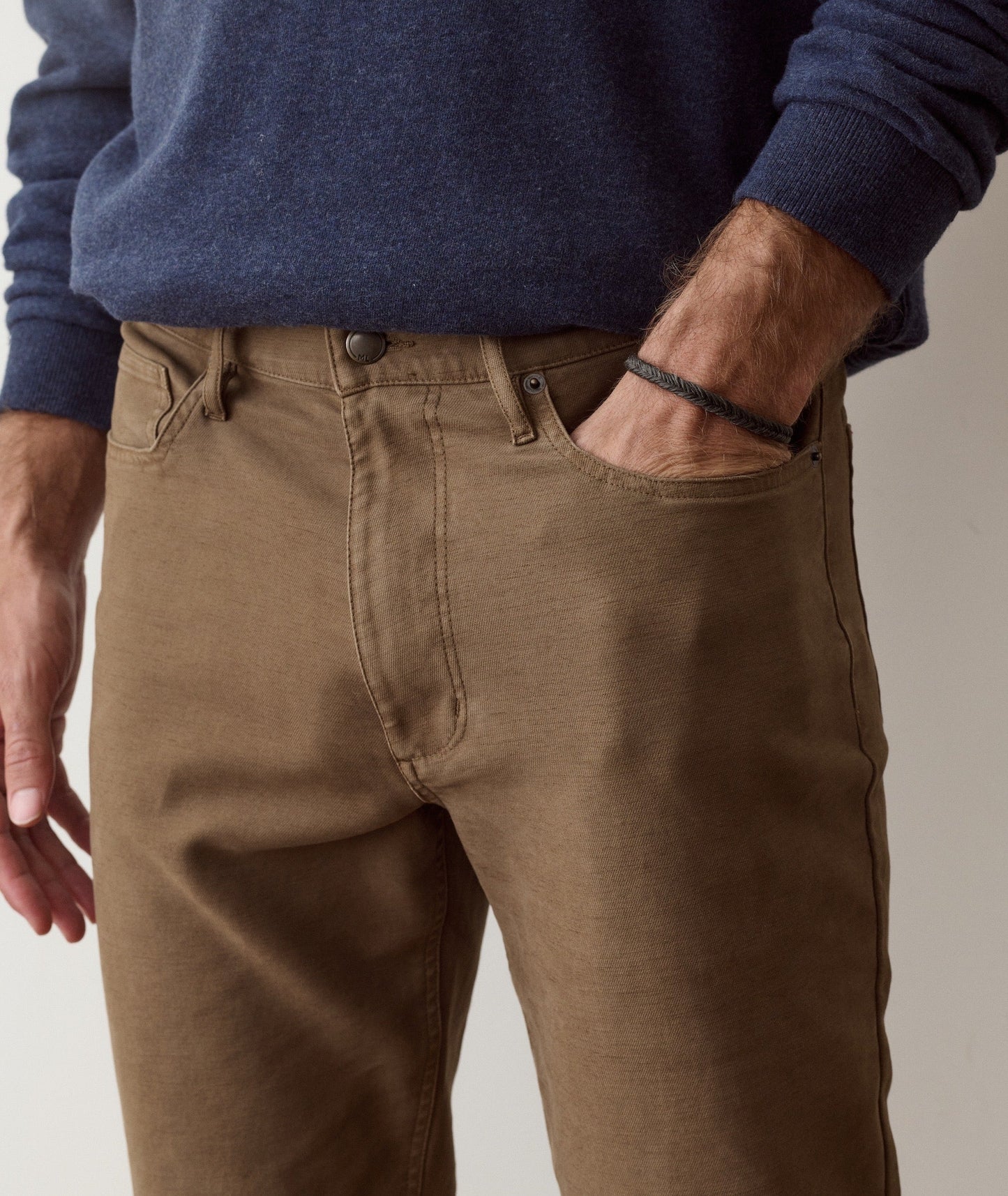 A close-up of a person wearing brown chino pants with a navy blue sweater, showing the front pocket and side pocket details.