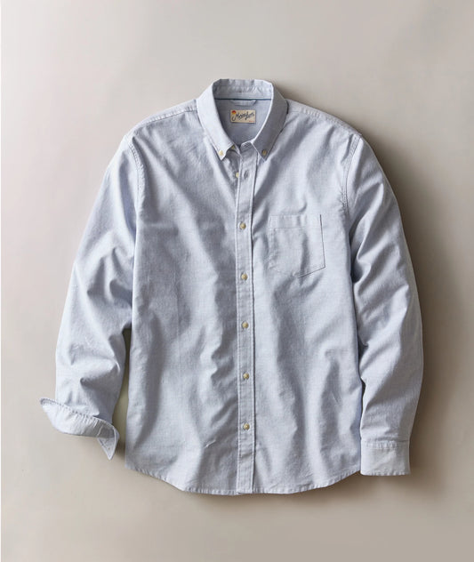 A light blue long-sleeve button-down shirt with a single chest pocket, laid flat against a neutral beige background.