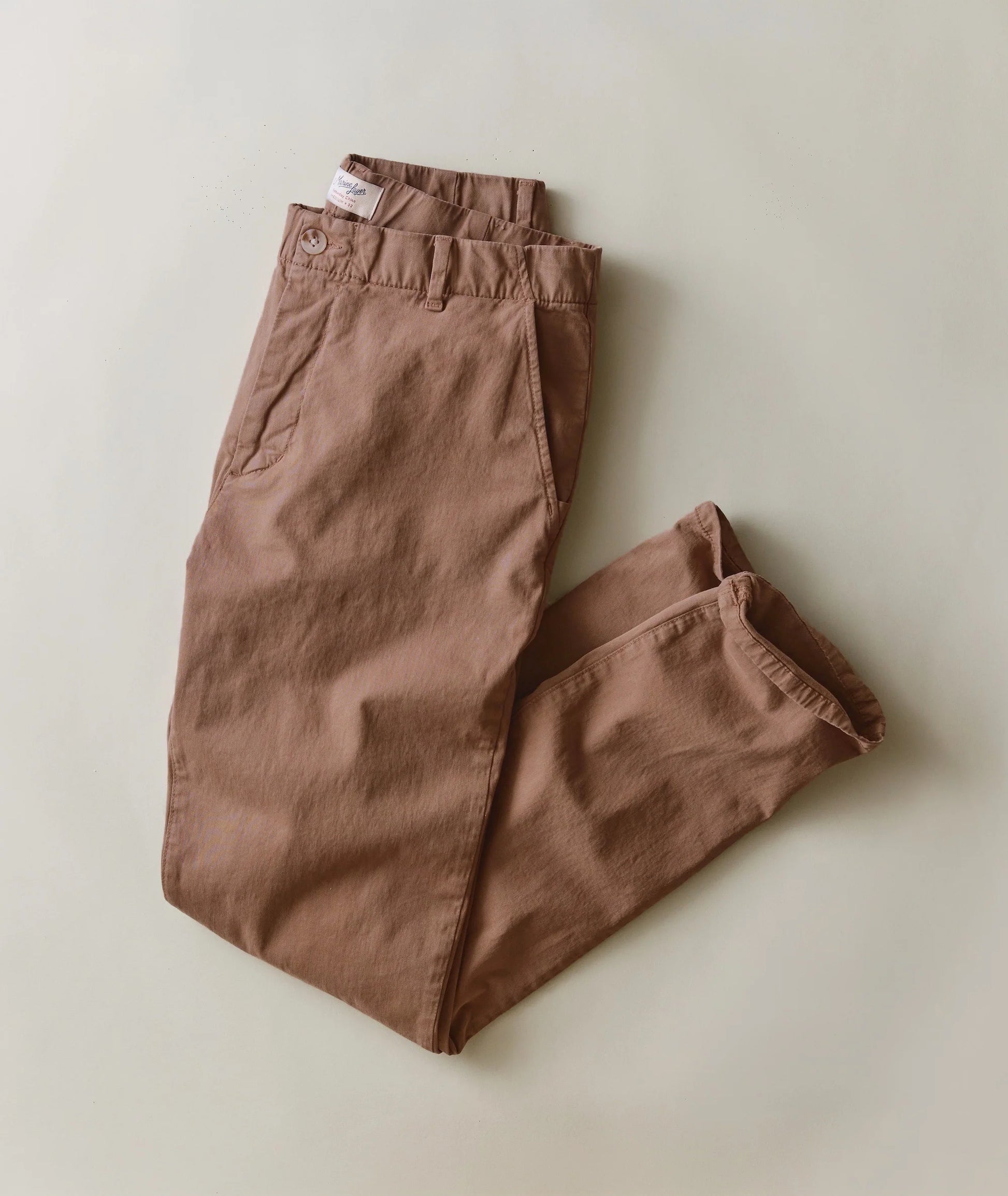 A pair of folded brown trousers laid flat on a light beige background.