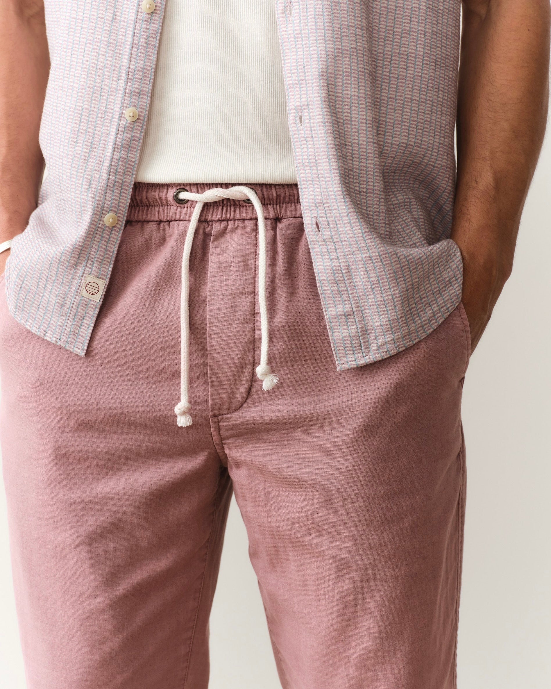 Person wearing mauve pants with a drawstring and a light-colored shirt with buttons.