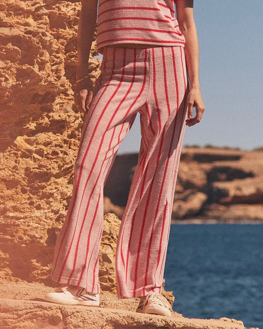 Person wearing red and white striped pants standing on a rocky surface with water and sky in the background