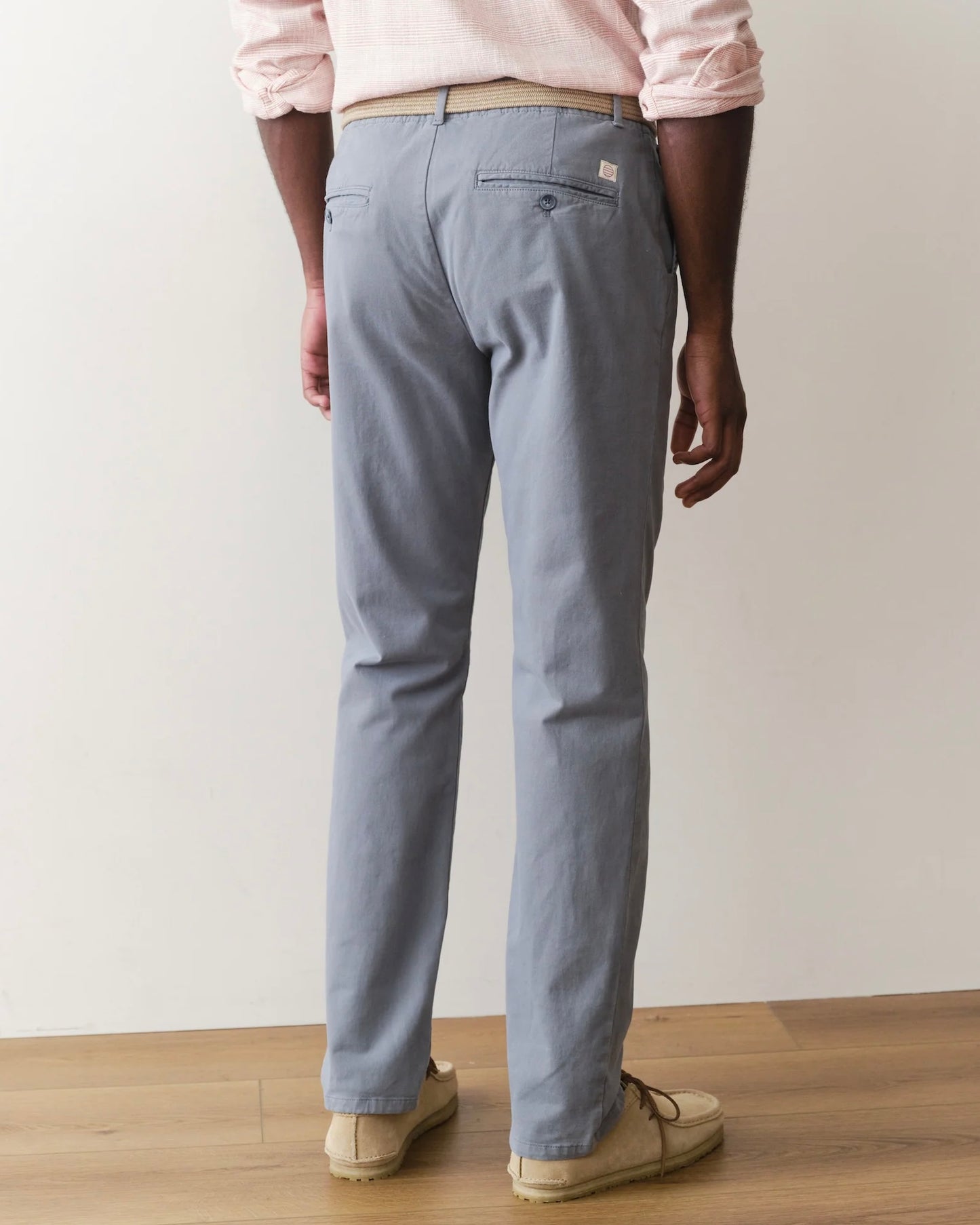 Person wearing light gray pants and a pink shirt on a plain background