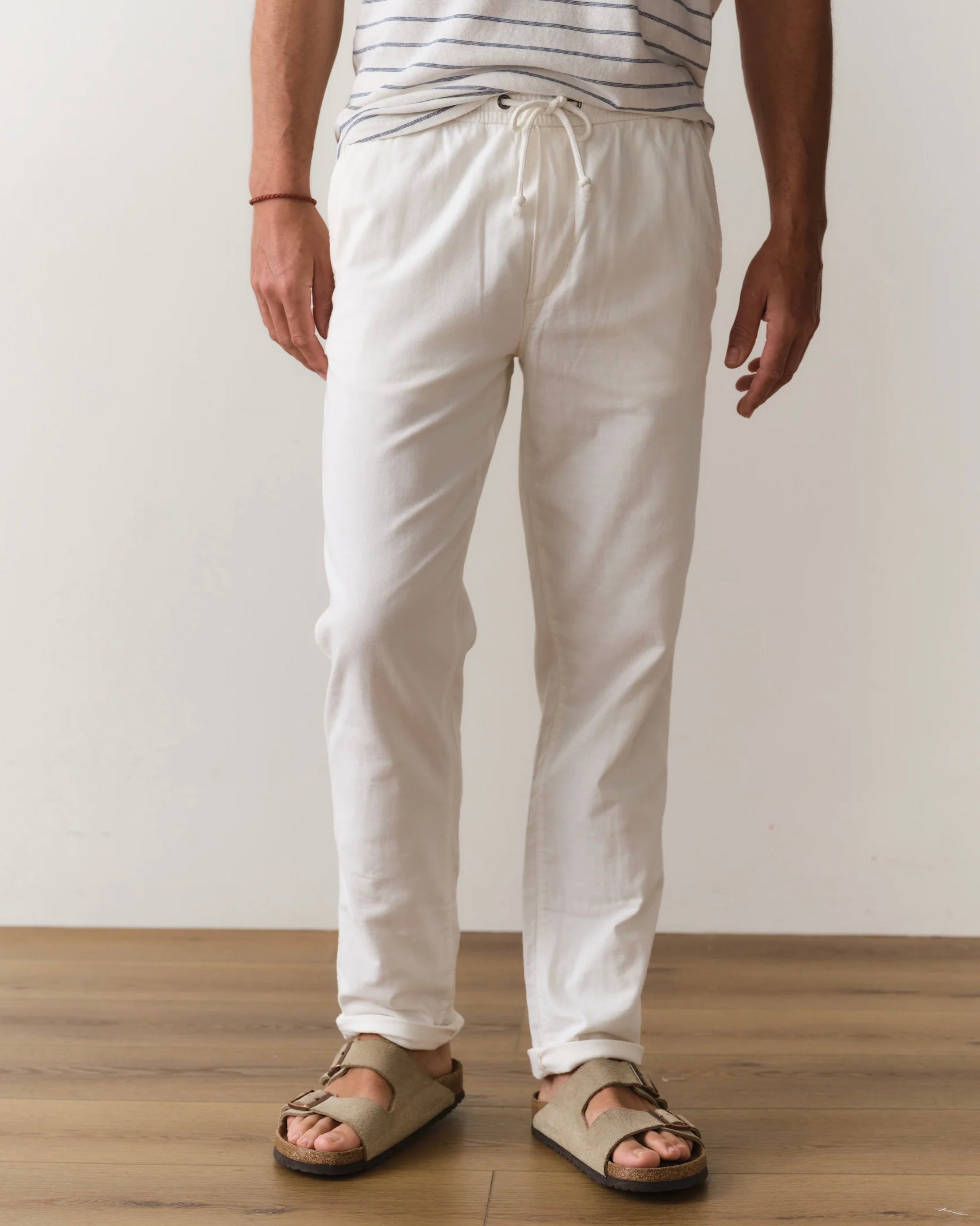 Person wearing white pants and sandals on a wooden floor with a plain background