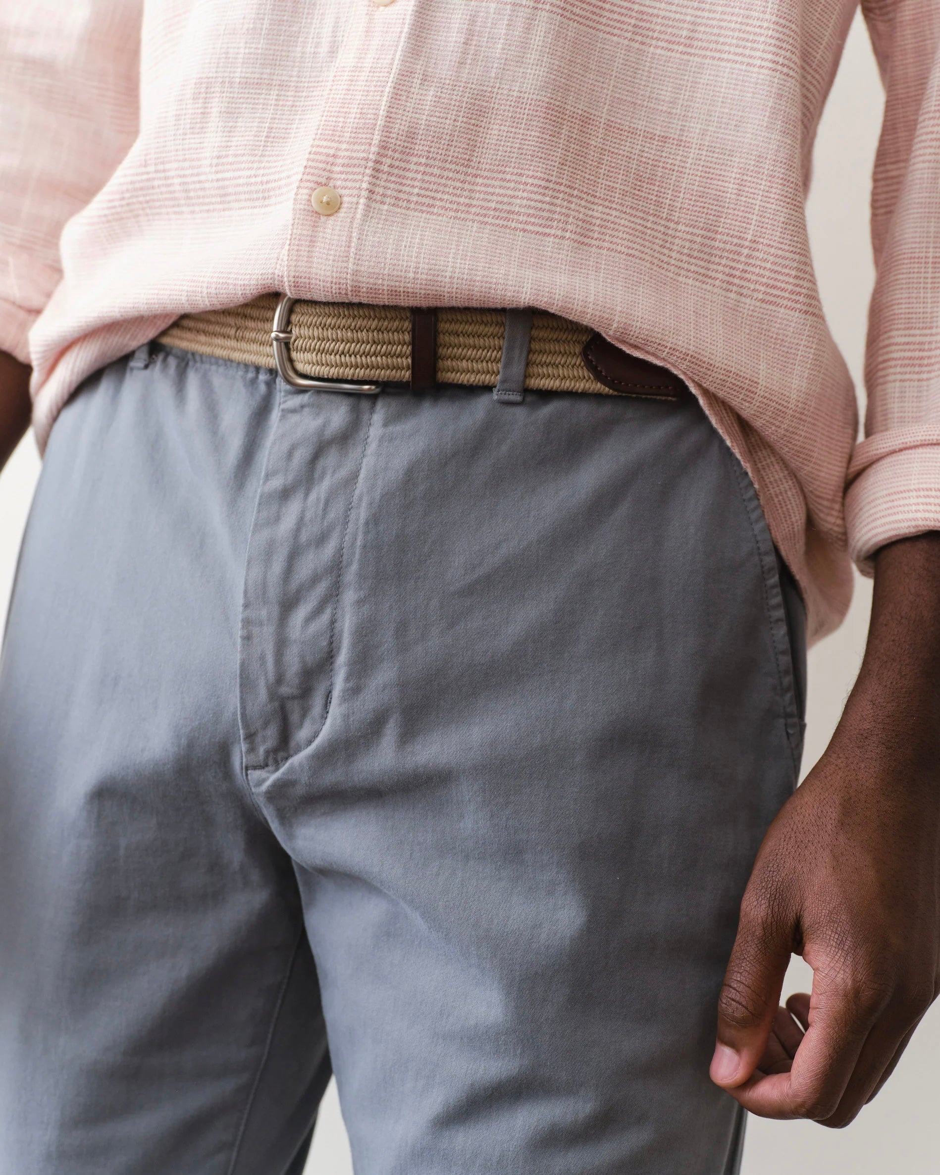 Person wearing a light pink shirt and gray pants with a beige belt.