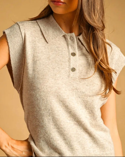 A woman wearing a dark gray sleeveless knit polo vest, posing against a solid warm brown studio background.
