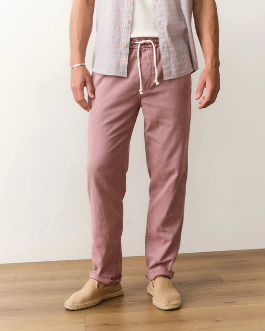 Person wearing pink pants and a light shirt on a wooden floor with a white wall background