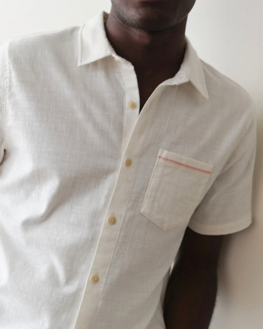 Man wearing a light-colored button-up shirt with a pocket against a neutral background
