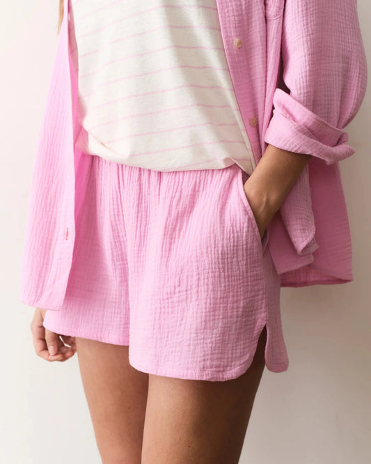 Person wearing a pink checkered shirt over a white top with pink shorts on a plain background
