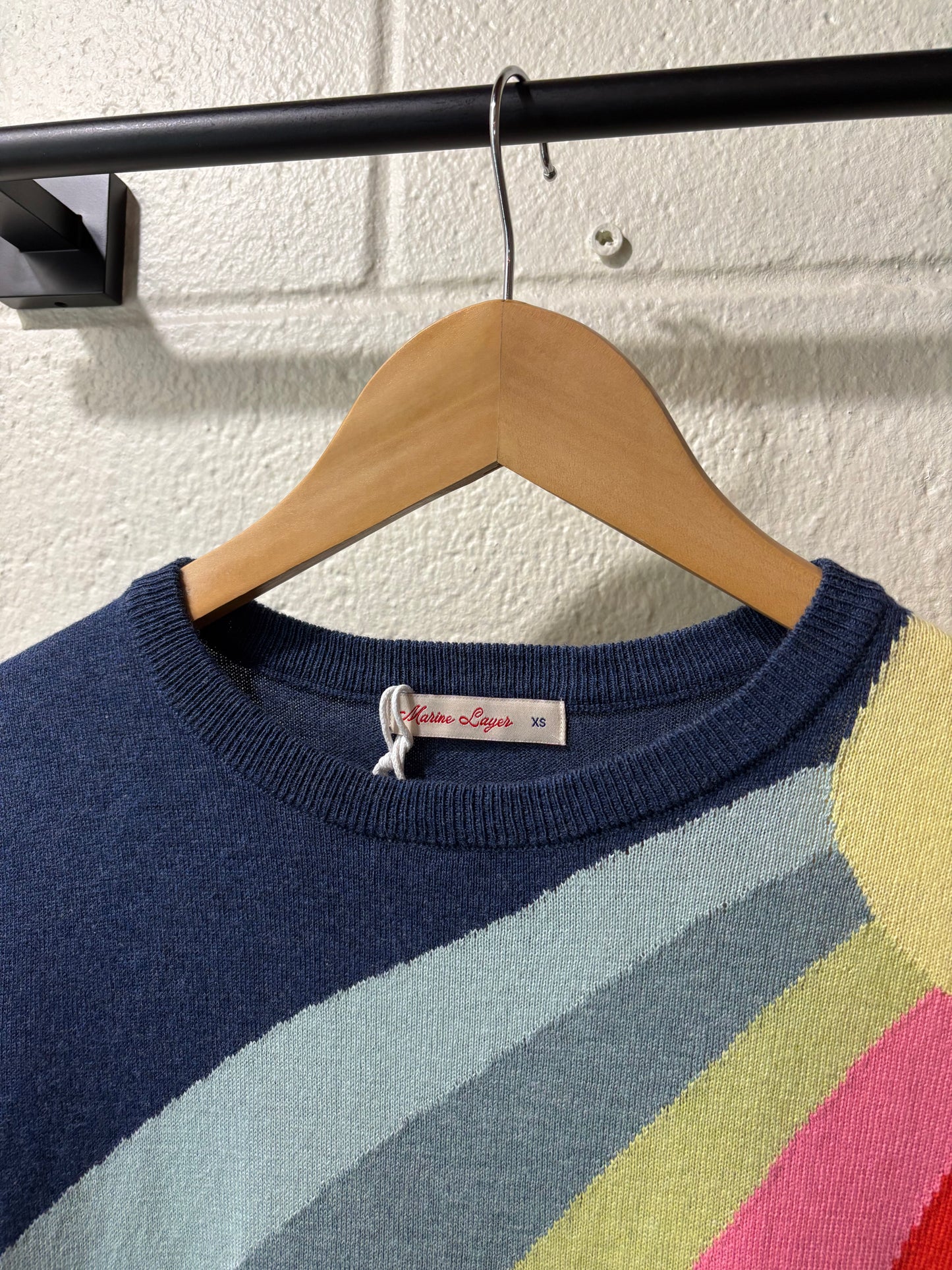 Colorful striped sweater on a wooden hanger against a white wall.