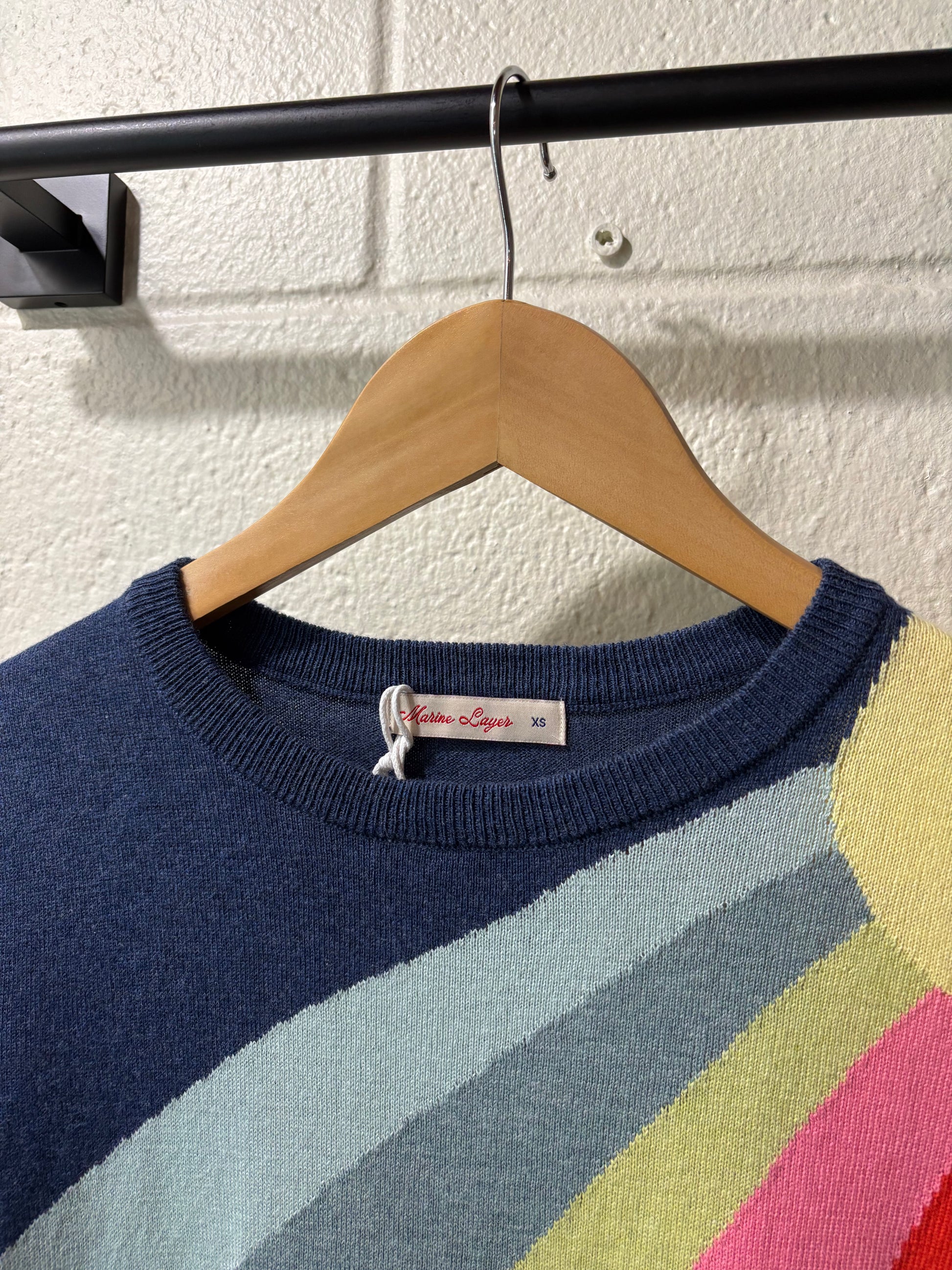 Colorful striped sweater on a wooden hanger against a white wall.