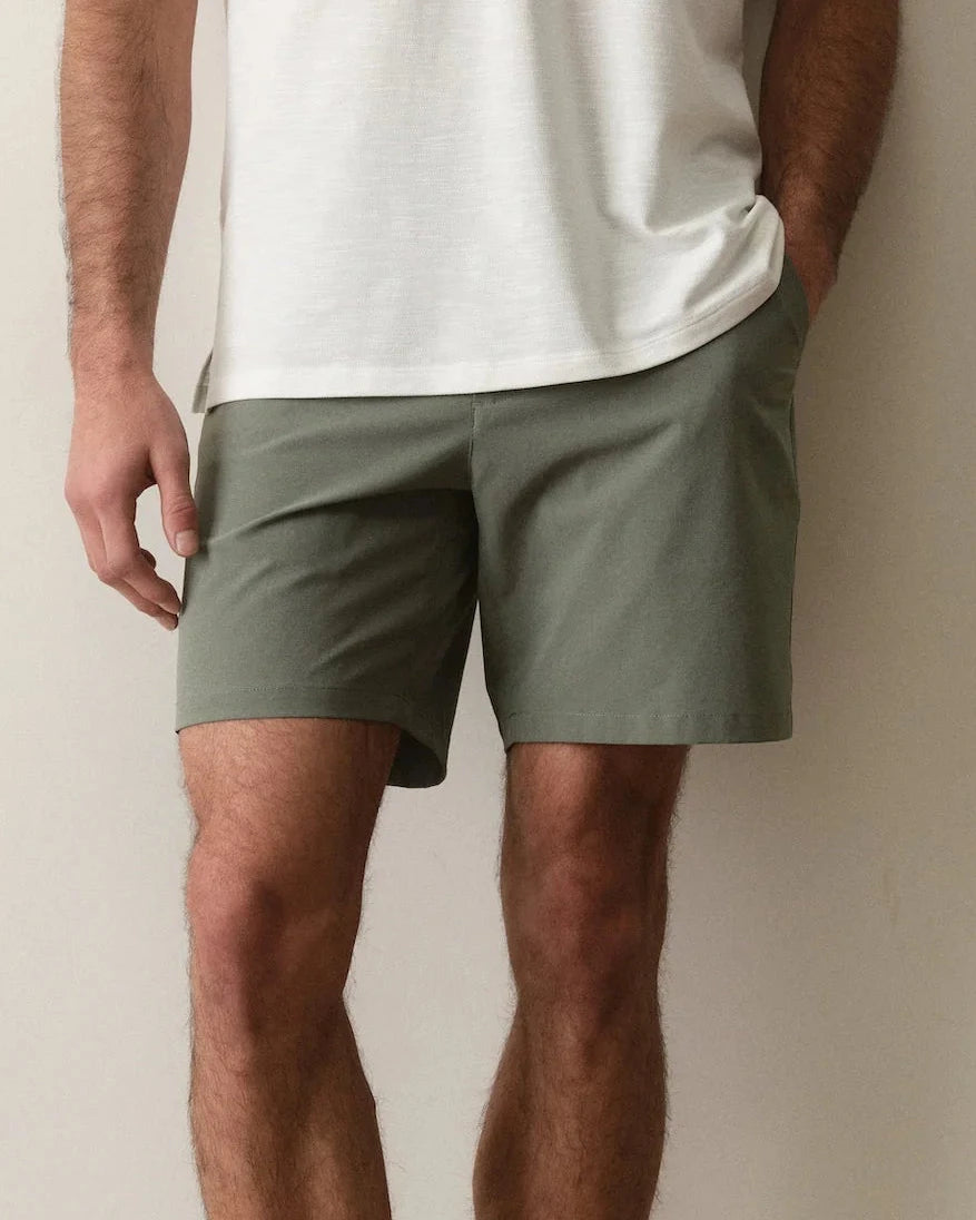 Man wearing a white polo shirt and green shorts against a plain background