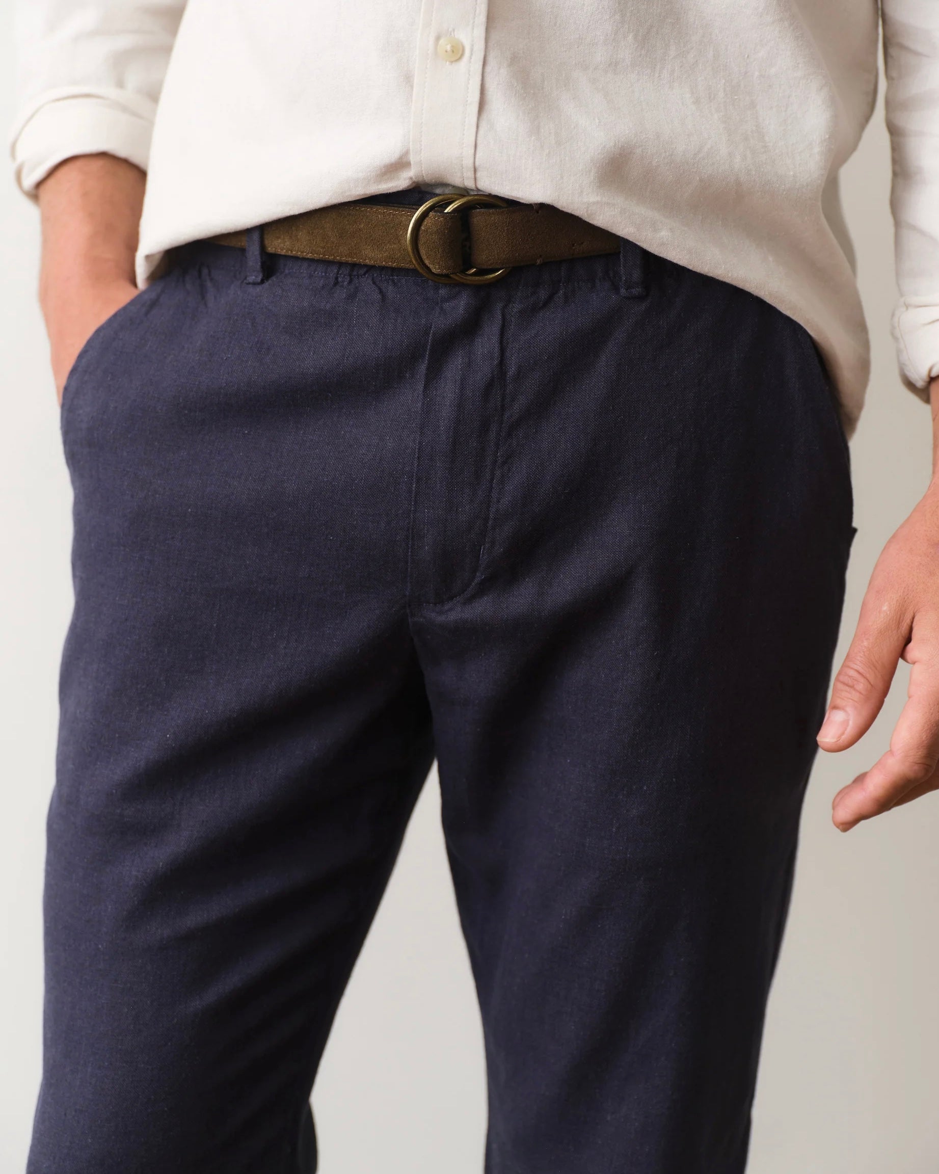 Navy pants with a brown belt worn by a person on a plain background