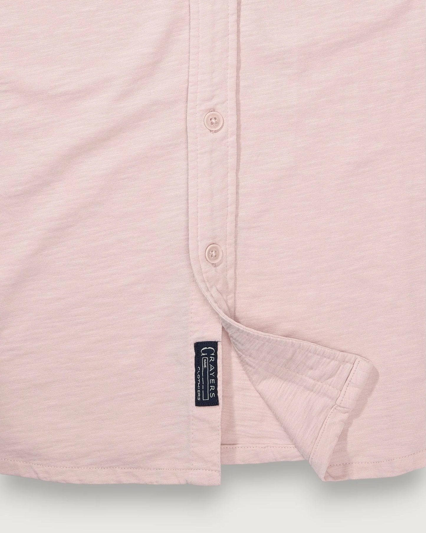 Close-up of a light pink shirt with a brand label on a light gray background