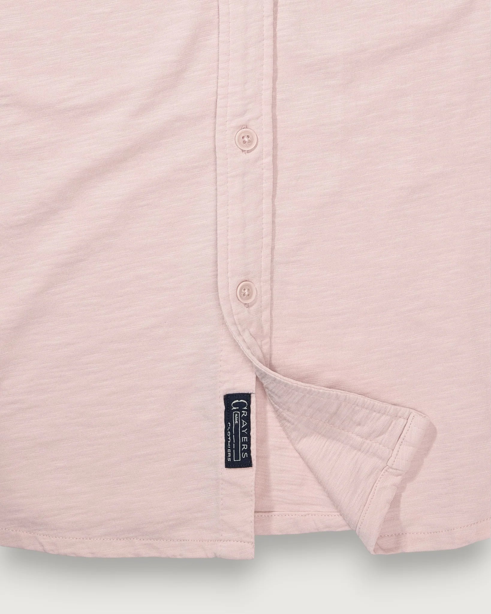 Close-up of a light pink shirt with a brand label on a light gray background