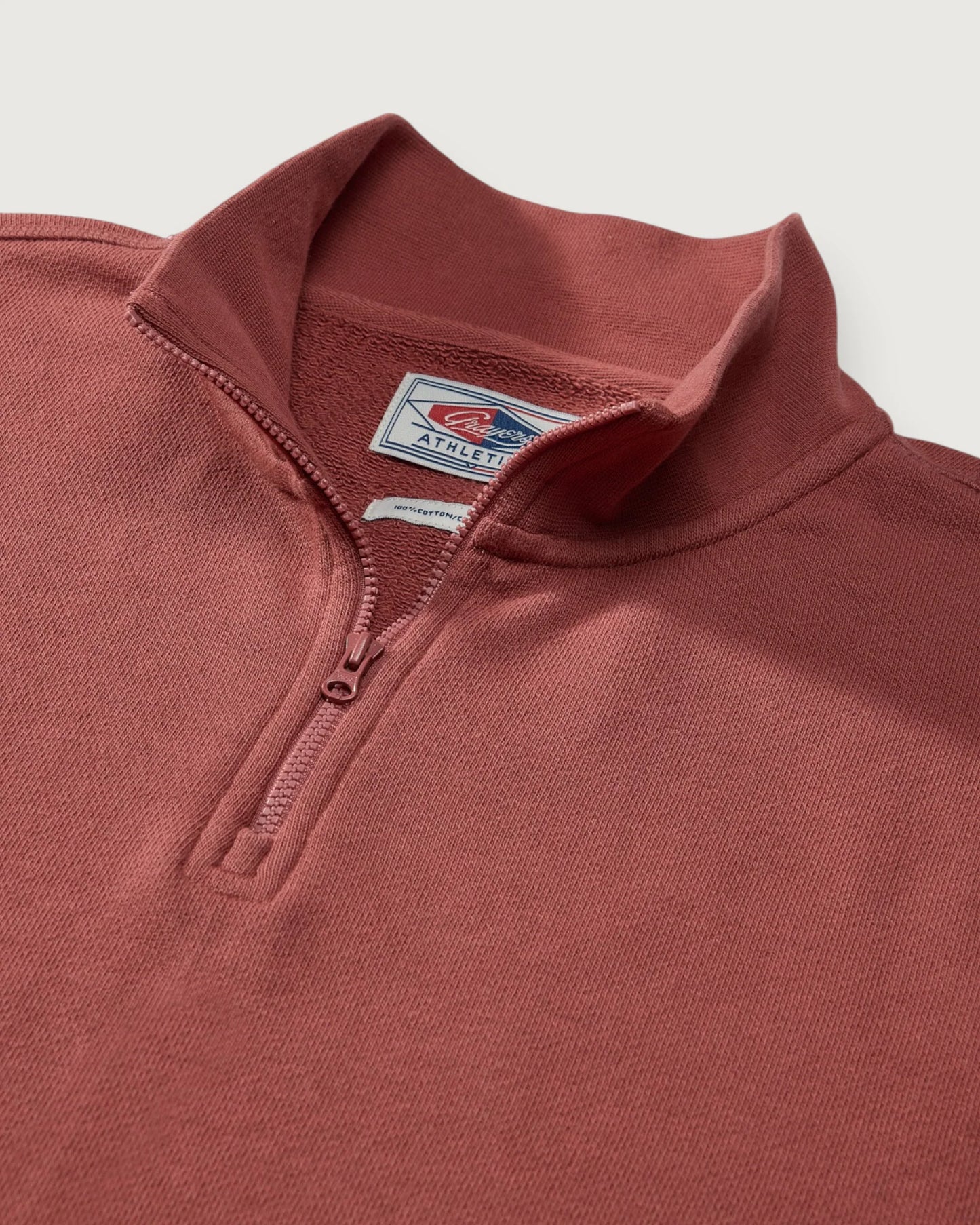 Close-up of a maroon pullover with a brand logo on a light gray background