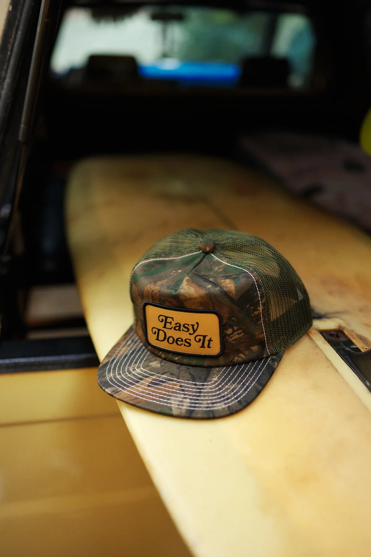 Camo cap with 'Easy Does It' patch on a car seat