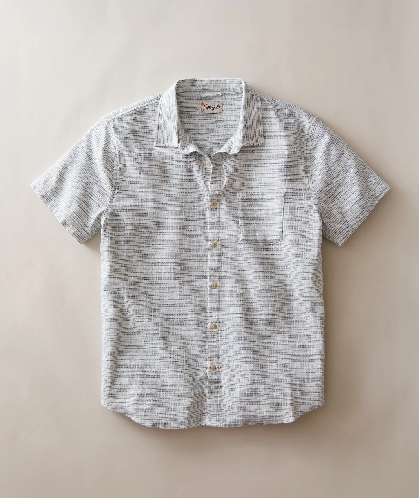 A short-sleeve button-up shirt with a subtle gray and white textured stripe pattern, laid flat against a solid beige background.