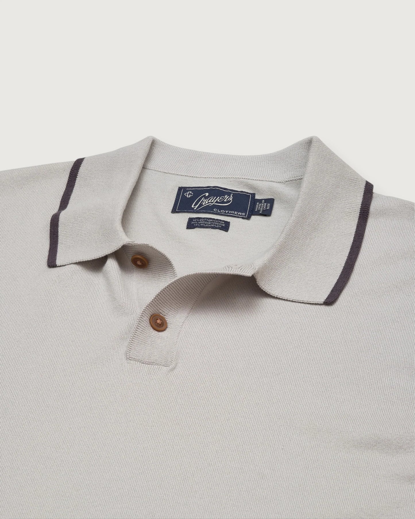 Close-up of a light gray polo shirt with a brand label on a white background