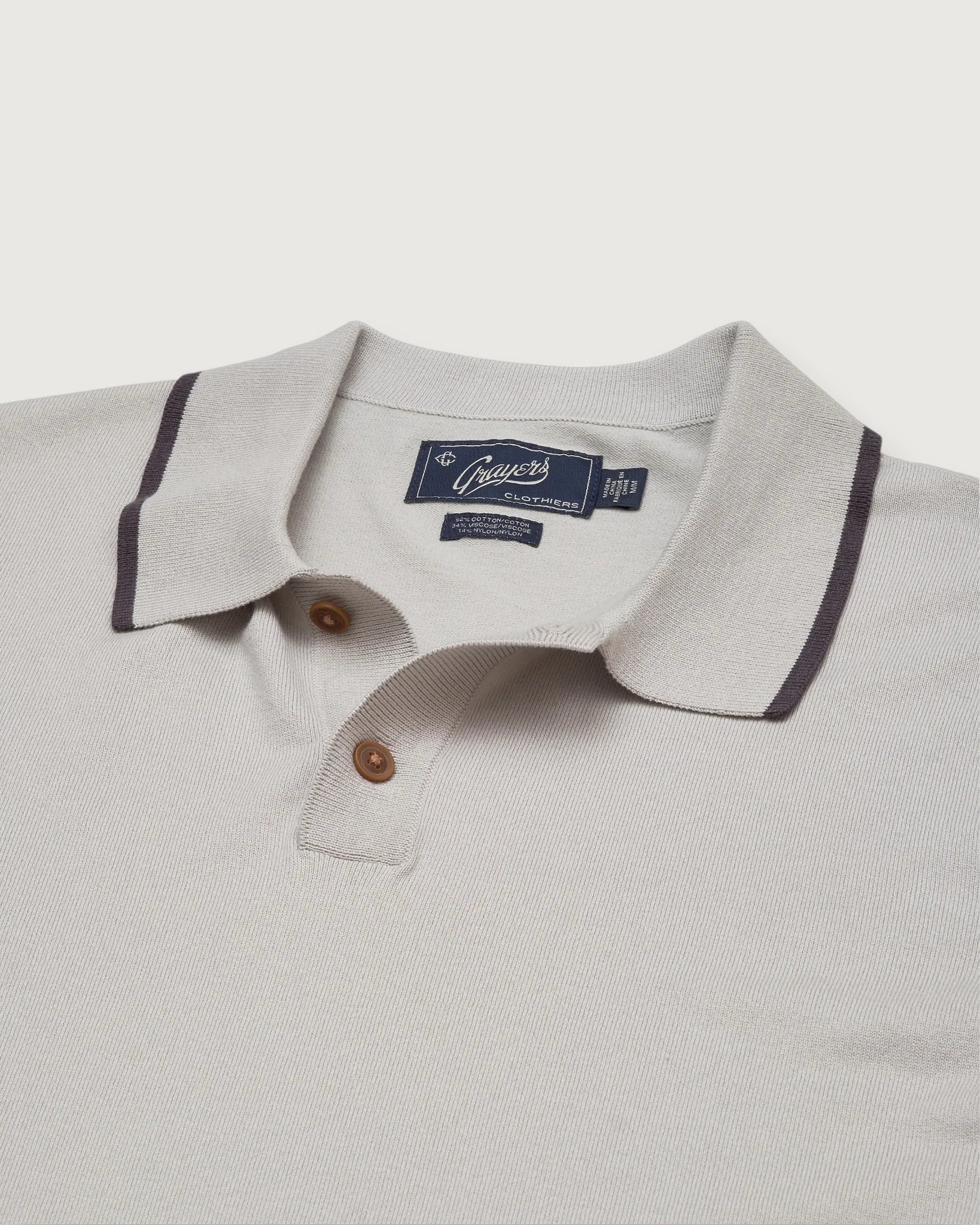Close-up of a light gray polo shirt with a brand label on a white background